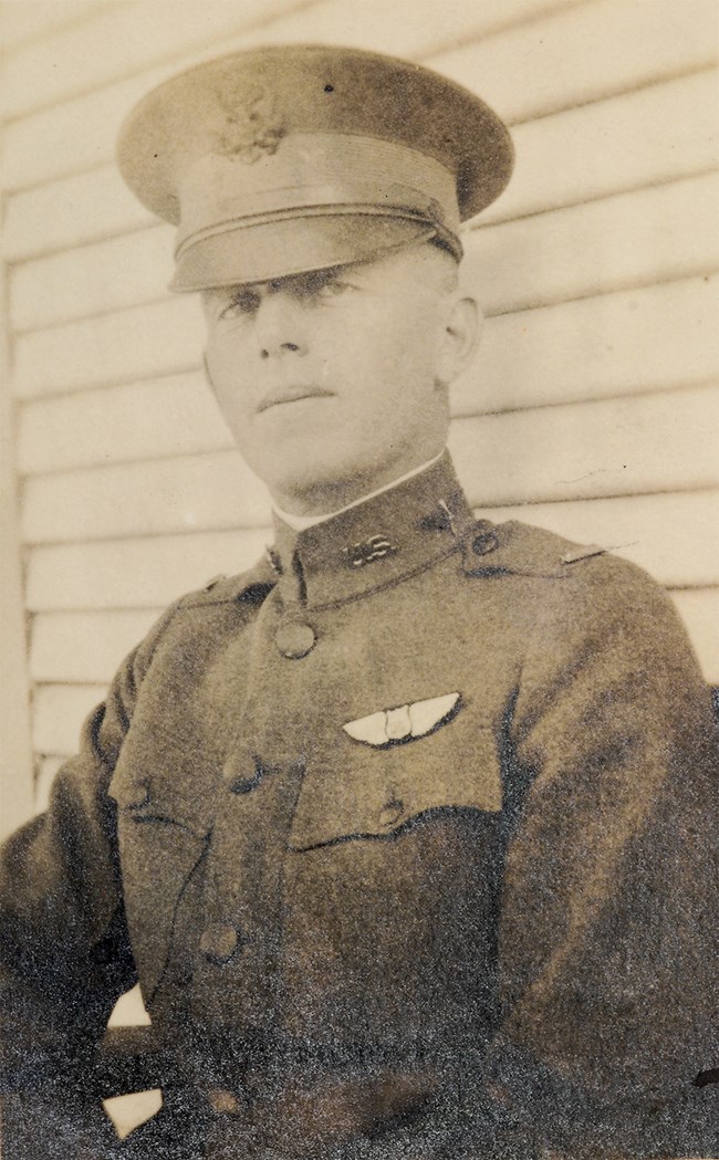 Black and white photo of a man in uniform. Pilot's wings insignia are pinned to his jacket.