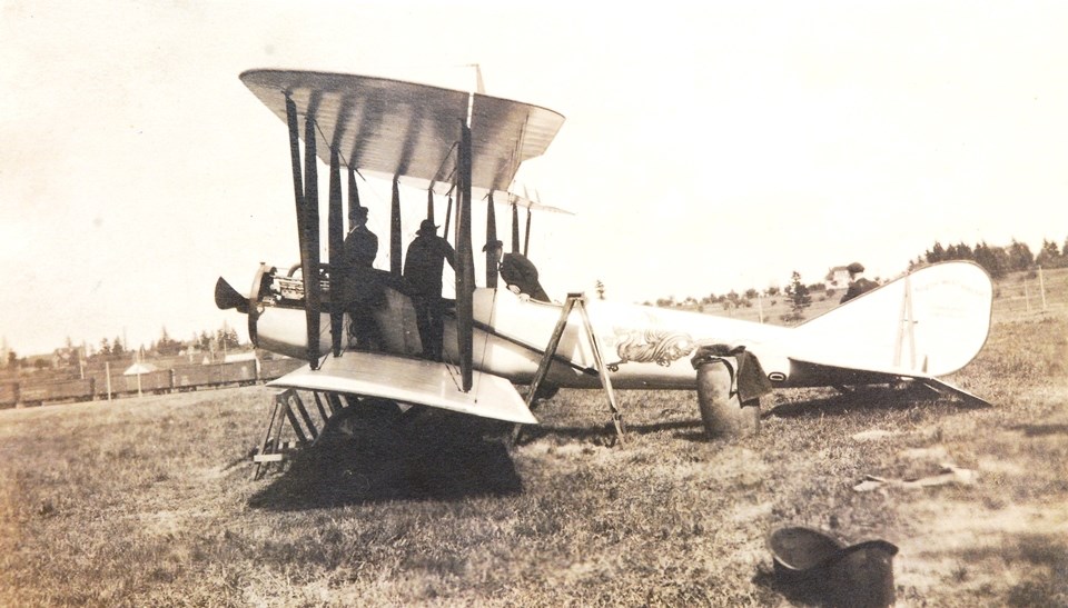 Photo of landed biplane. Three men look inside cockpit. A dragon is painted on the fuselage, and the tail is marked with "Northwest Aircraft Corporation Portland Oregon"