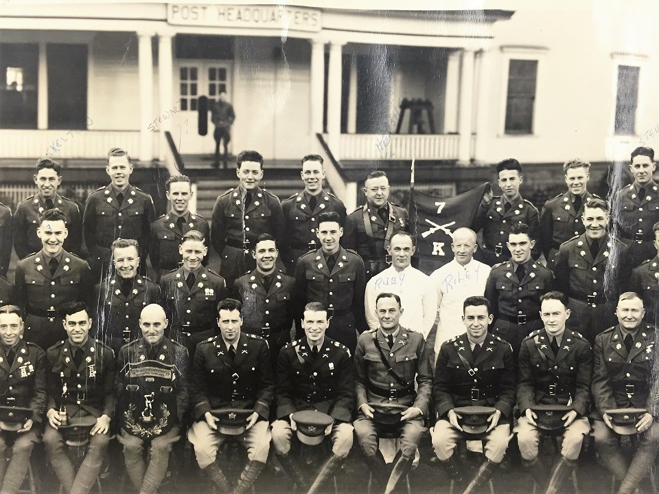 Black and white photo of a group of soldiers sitting and standing in front of a building with a sign reading "Post Headquarters."