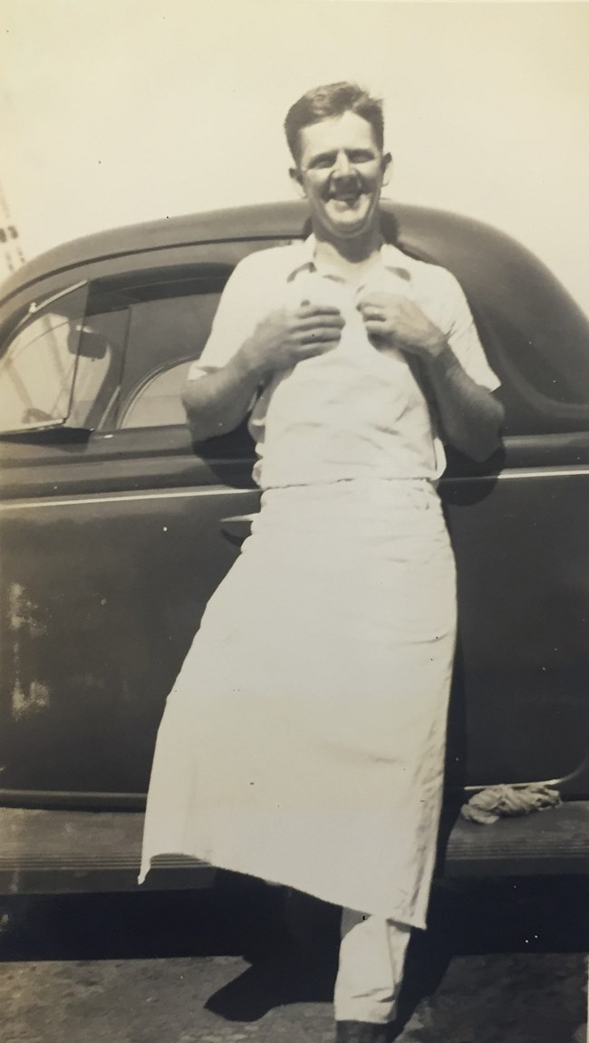 Black and white photo of a man wearing a white bakers smock.