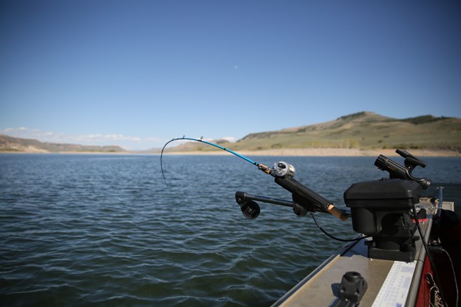 A fishing rod sits in a rod holder on the gunwale of a boat that is trolling. The rod is bending toward the water and is also attached to a downrigger.