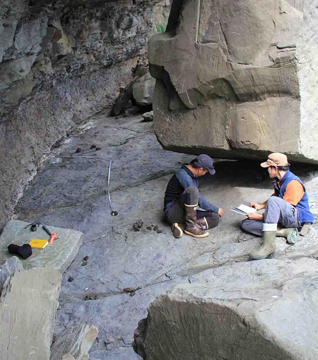 Two paleontologists work on a rocky ledge.