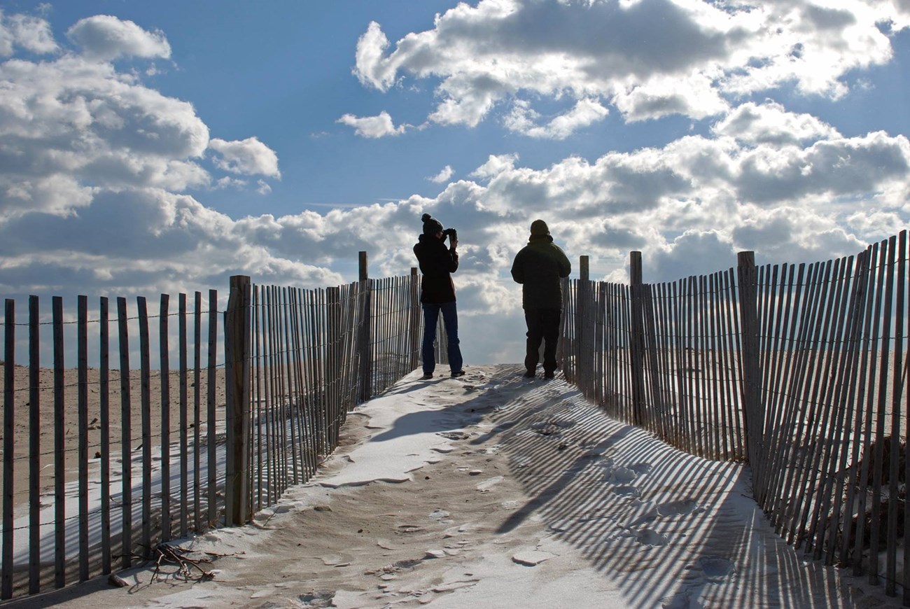 lt= two people stand on a dune overlooking the ocean
