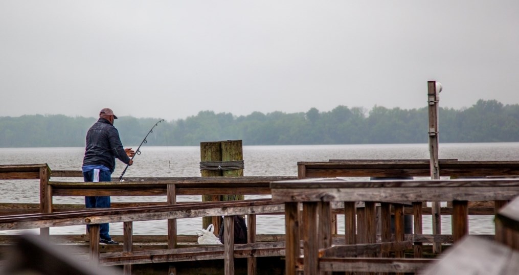 A man casts a fishing reel off of a dock in Piscataway Park on a cloudy day..