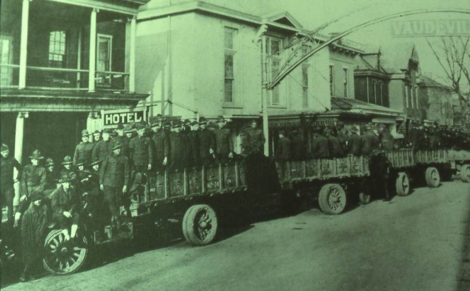 Many soldiers in the backs of heavy trucks awaiting transport