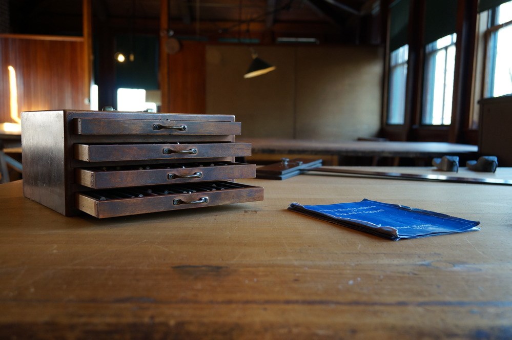 Close up of a desk with a box containing semi-open drawers and a blue book sitting on top.