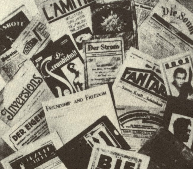 B&W photo of print periodicals with ink images and words piled together.