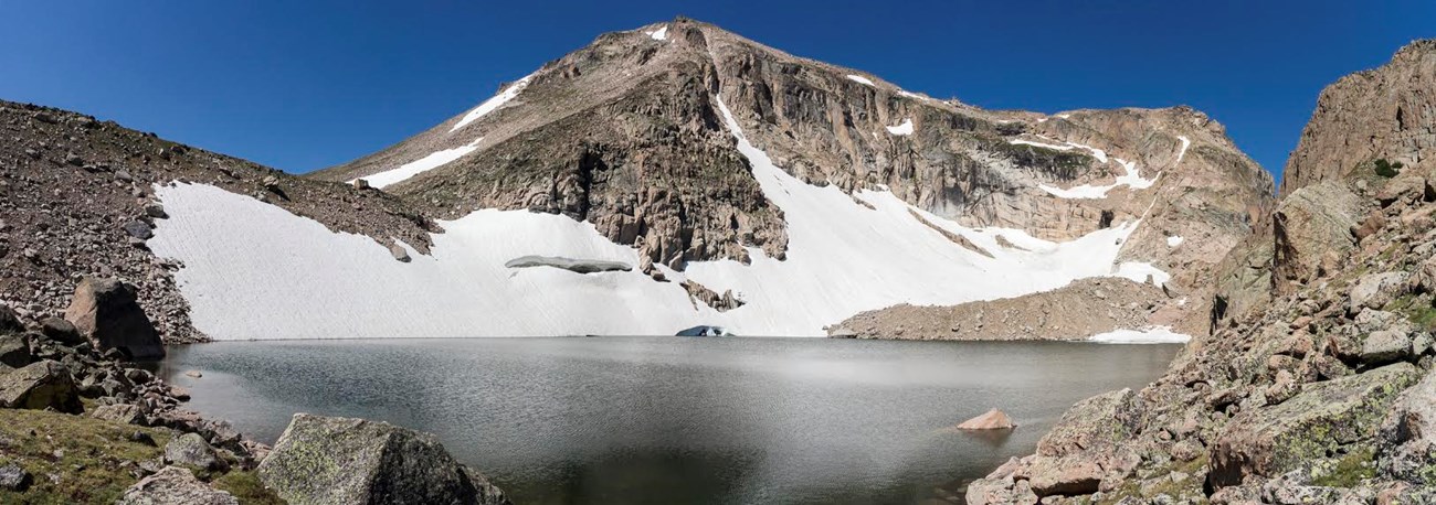 A pyrimid shaped peak and glacier above an alpine lake.