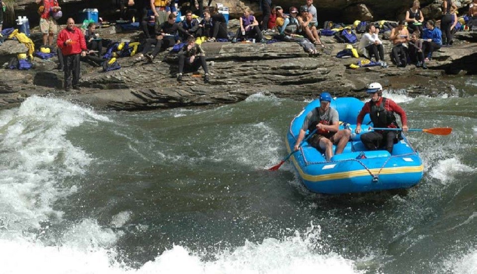 Whitewater paddlers setting up for a rapid while people watch from the shore