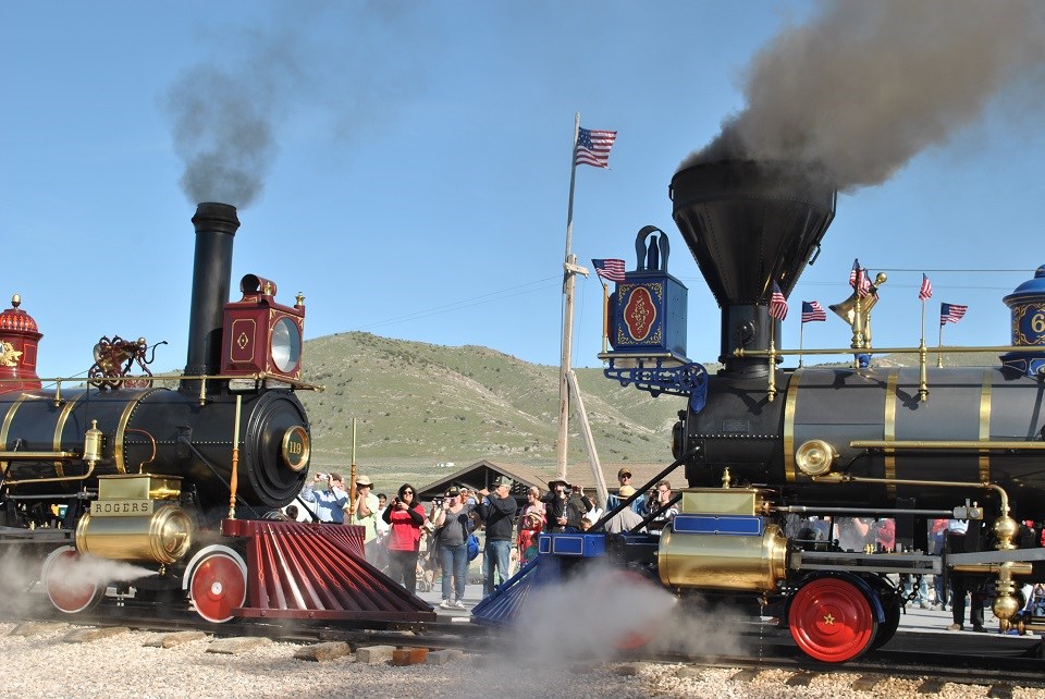 Two steam engines facing each other on a railroad track with a crowd watching