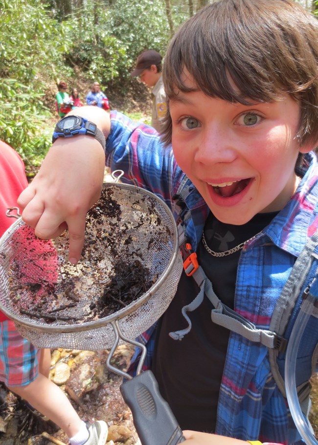 A young child excitedly points out a dragonfly larva in net.