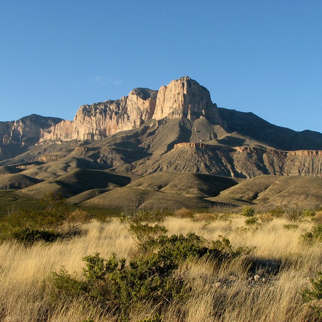 A tall rocky mountain face above a desert valley floor