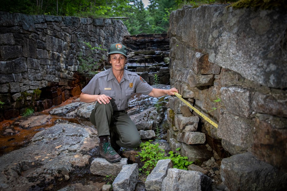 Woman in uniform holds a tape measure to a stone wall