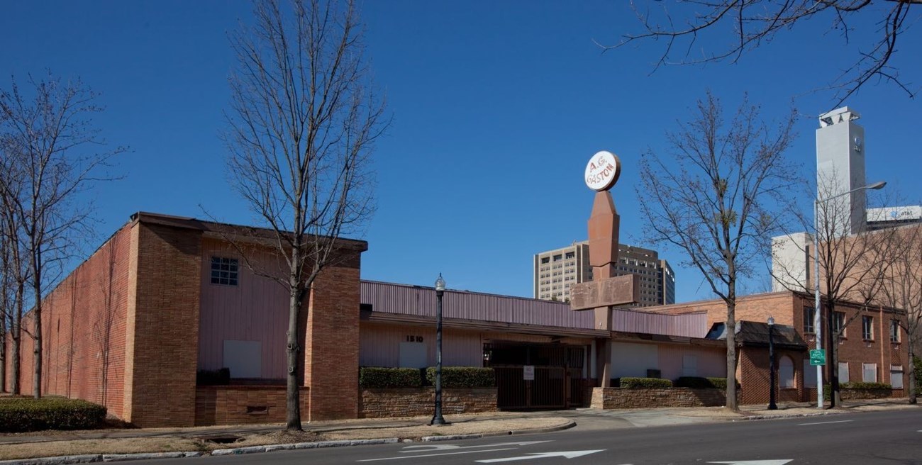 A.G. Gaston Motel is rectangular building with low stone wall along the front and trees along the sidewalk