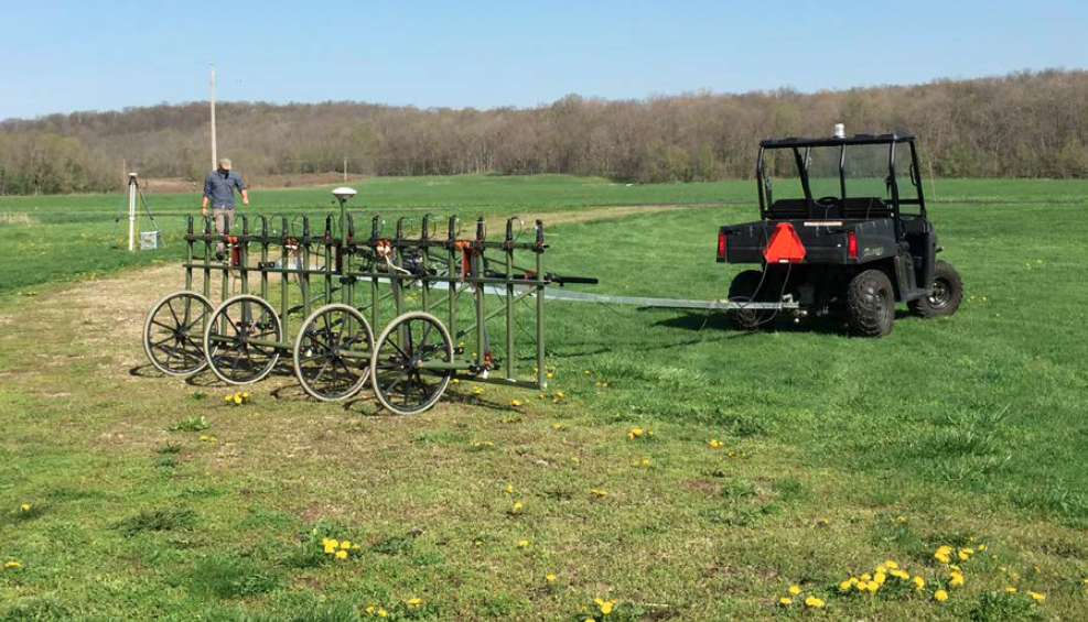 Geomagnetic Array An atv vehicle attached to a trailer with several small instruments in a green field