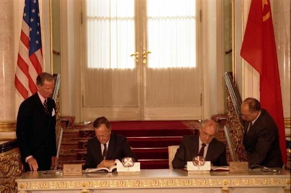 Presidents Bush and Gorbachev sign a treaty while seated at a table.