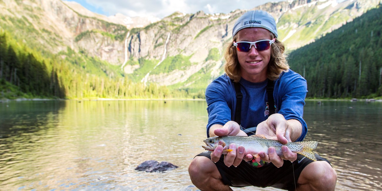 Cutthroat in Glacier A man squats near a lake with a fish in his hands
