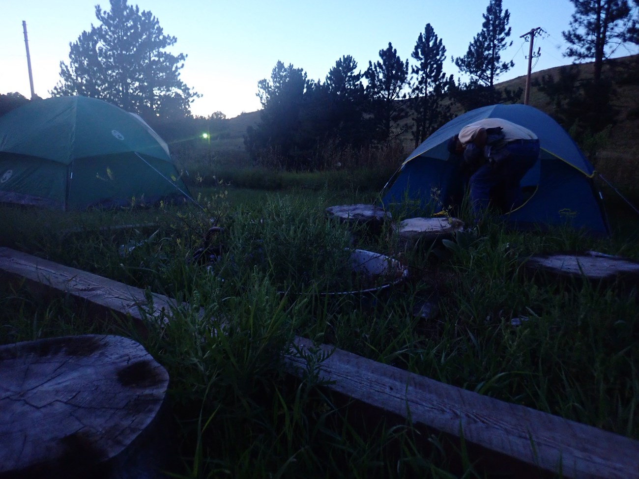 A pair of tents sitting next to a firepit just after sunset.