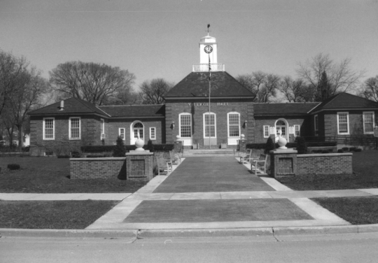 B&W photo of a brick building with a small court and flagpole in front.