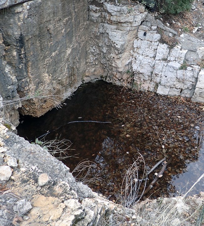 A square-shaped pool of water surrounded by bedrock faces on three sides