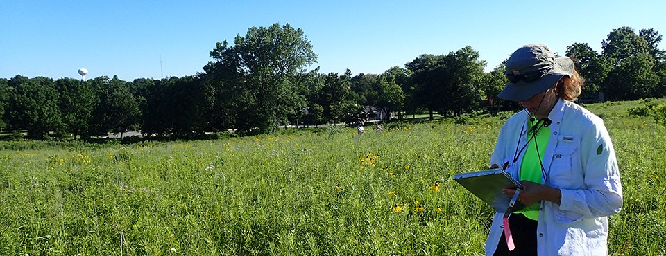 A woman with a notebook stands on a prairie.