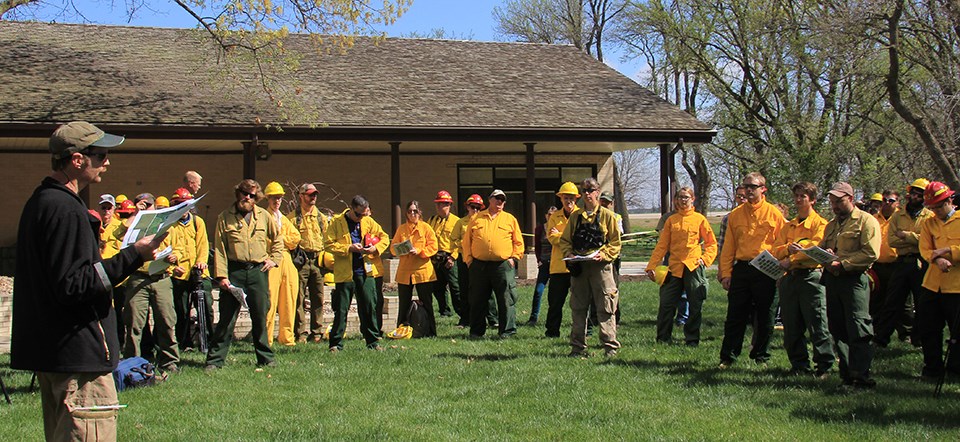 A man stands in front of a group of men and women in firefighting gear.