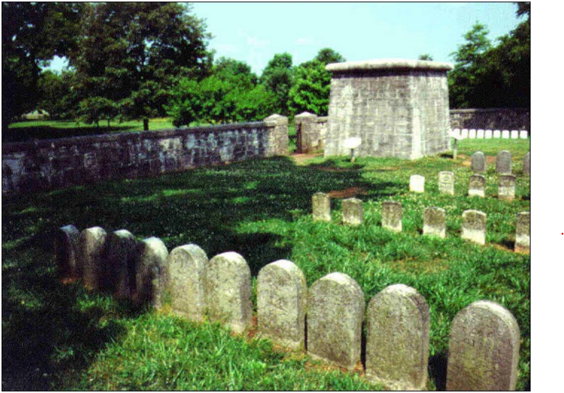 Gravestones and a stone structure in a yard bordered by a stone wall