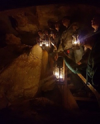 People with lanterns lean over a stair rail in a cave