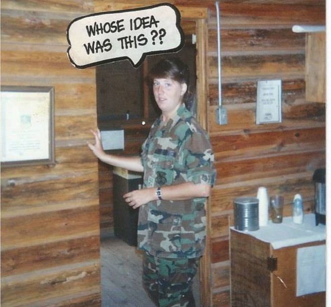 woman in airforce fatigues stands in a doorway