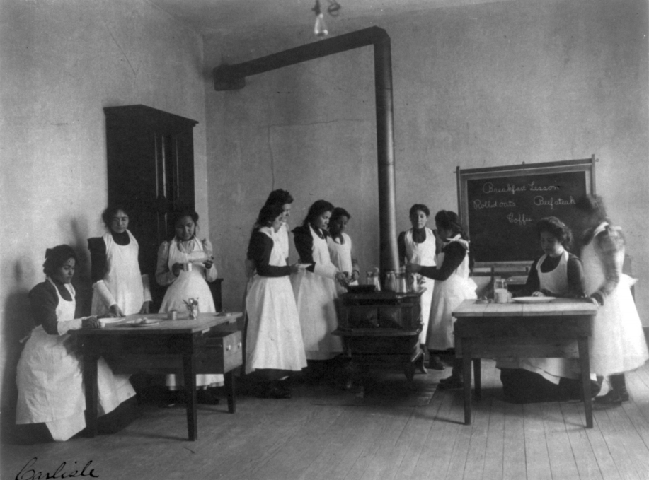 Girls cooking. They are all wearing aprons.