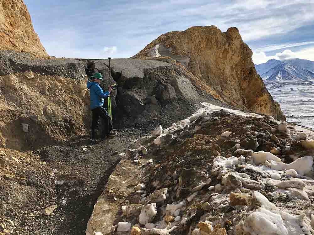 A researcher stands below the road grade where the road has slipped.