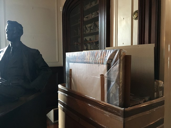 A crate of wrapped paintings next to a large bronze sculpture of FDR.