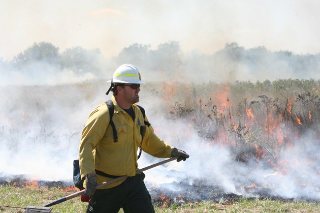 Firefighter walks on a fireline next to a burning prescribed fire in the tallgrass prairie