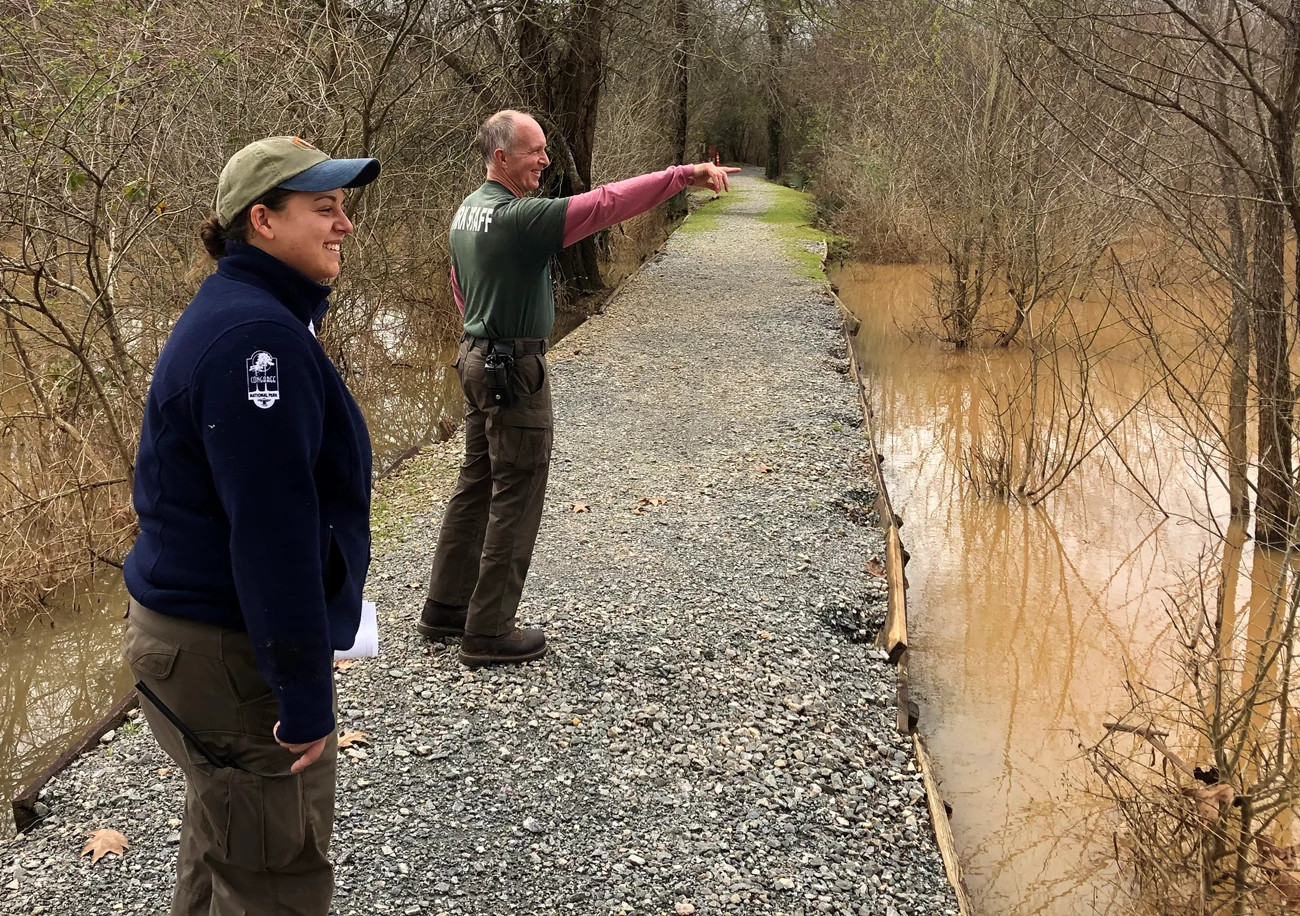 Looking for a native vegetation restoration site at OCMU. Man and woman stand on a road near water pointing to the right.
