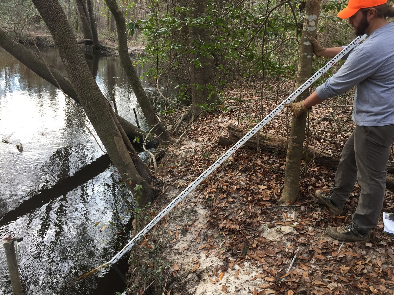 Man stands with a measuring rod on the banks of a stream.