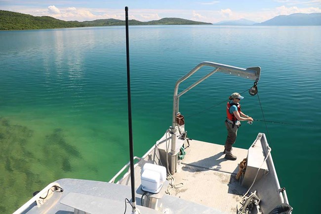 A researcher fishes in a lake from a boat.