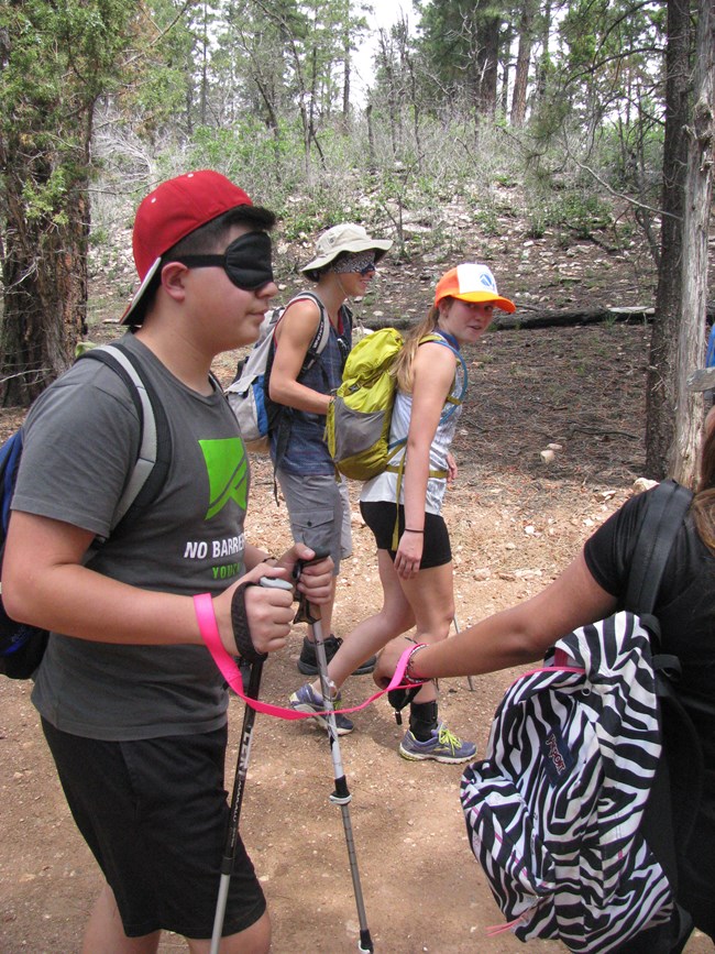 A blind folded, sighted teen is led by a visually impaired youth in a Leading the Way program exercise on the trail at Grand Canyon.