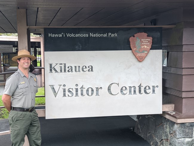 Kekoa Rosehill in National Park Service uniform by a sign that says "Kilauea Visitor Center"