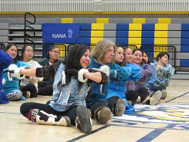 Traditional dancers sit on the gym floor.
