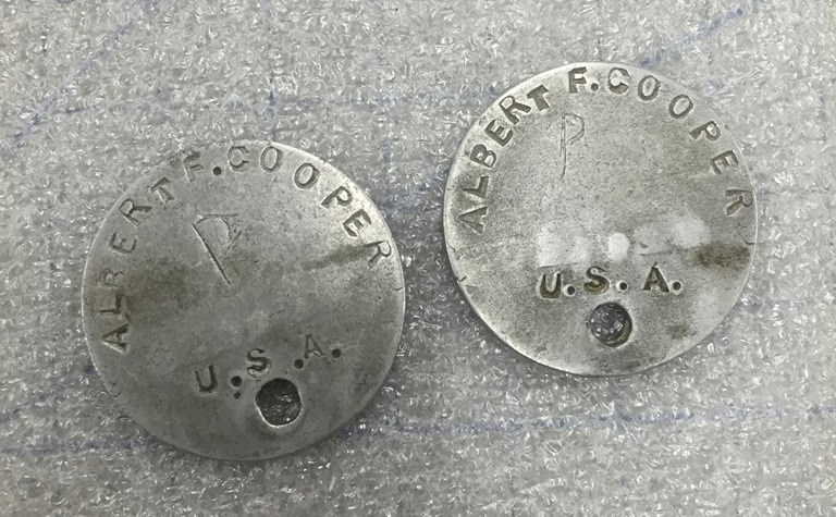 Photo of two round aluminum dog tags with Albert Cooper's name