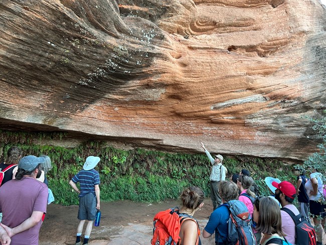 Nick Nyquist A park ranger surrounded by a crowd of people point to a large rock all