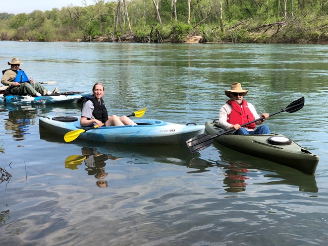 3 paddlers on the water in green kayaks wearing pfd's with paddles