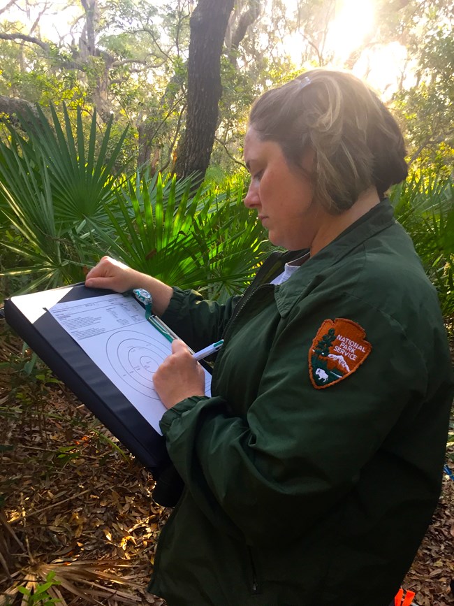 A woman writes something on a clipboard she is holding.