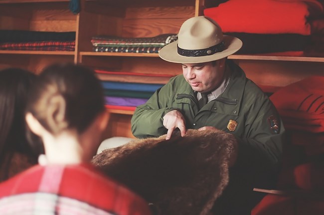 Park ranger holding up a fur in front of a wall displaying blankets