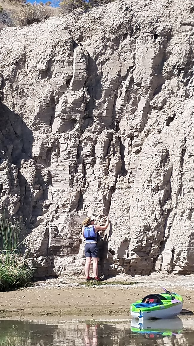 Image 2 hafo person and kayak on narrow beach at the base of a bluff
