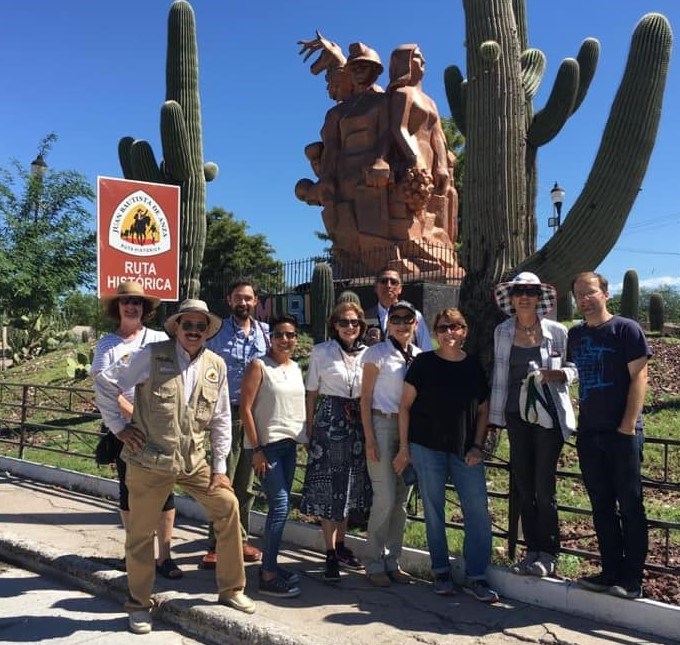 A small group of people posing for a photo in front of cacti and a statue