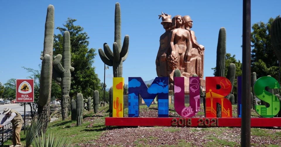 A colorful sign spelling IMURIS in front of a civic statue in a desert landscape