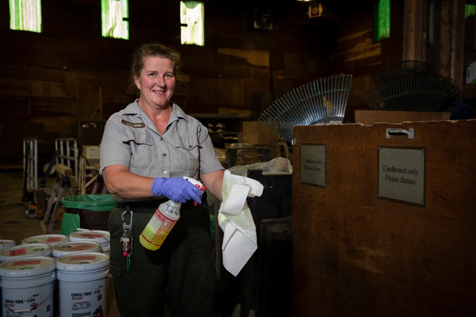 Woman wearing blue work gloves holds rags and a spray bottle