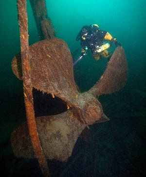 Diver with flashlight swims near large propeller. Diver with flashlight swims near large propeller.