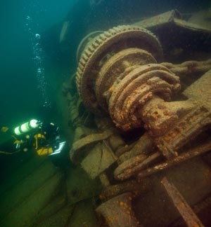 Diver with notepad swims near submerged machinery. Diver with notepad swims near submerged machinery.